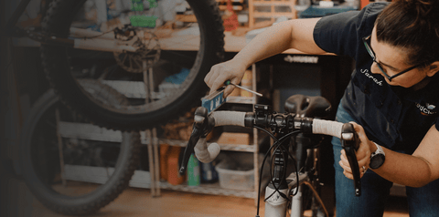 alt=" Sarah Pushee owner of Red Clover Bikes, adjusting a customer's handlebar."