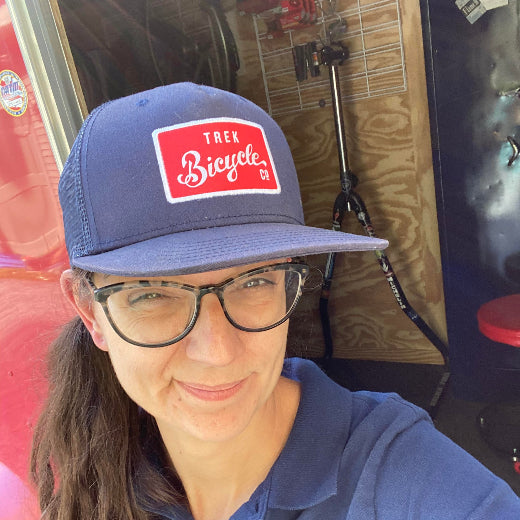 Sarah Pushee, Owner wearing a blue cap with a bicycle brand logo, standing in front of a vehicle.